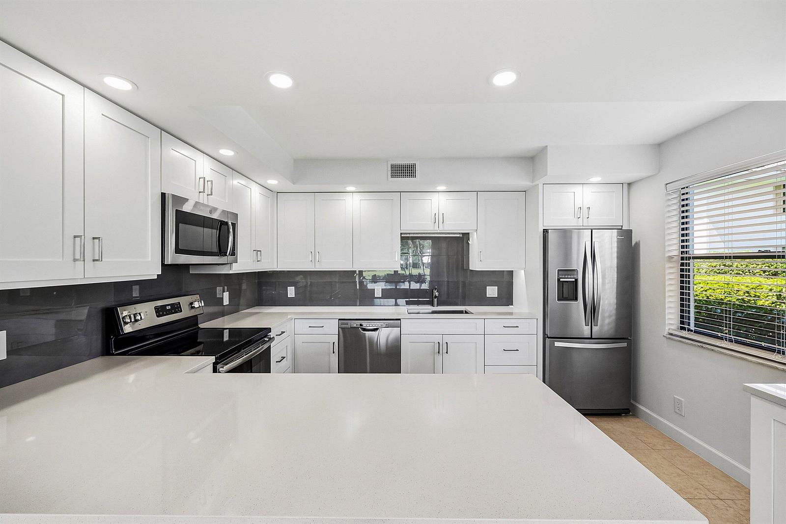 A modern kitchen features white cabinets, stainless steel appliances, and a large quartz countertop island — 3682 Quail Ridge Drive N, Boynton Beach FL 33436, BOYNTON BEACH, FL