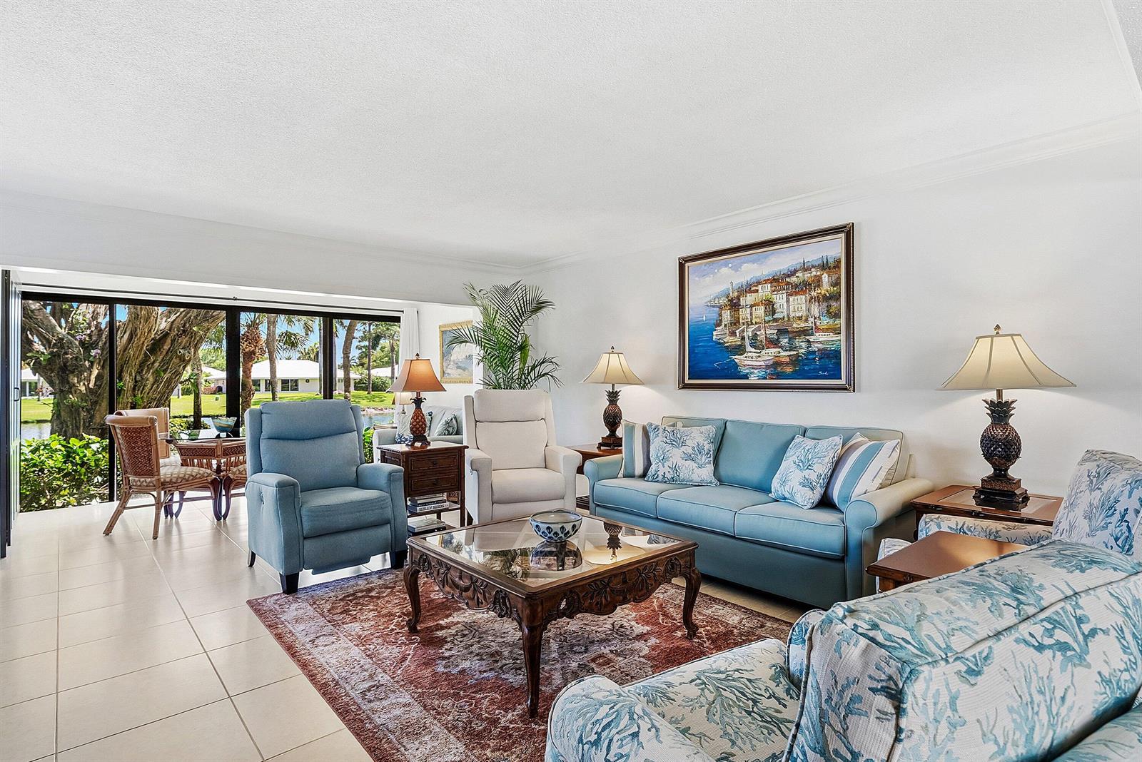 A living room features a blue sofa, matching armchairs, a patterned rug, and large sliding doors — 3682 Quail Ridge Drive N, Boynton Beach FL 33436, BOYNTON BEACH, FL