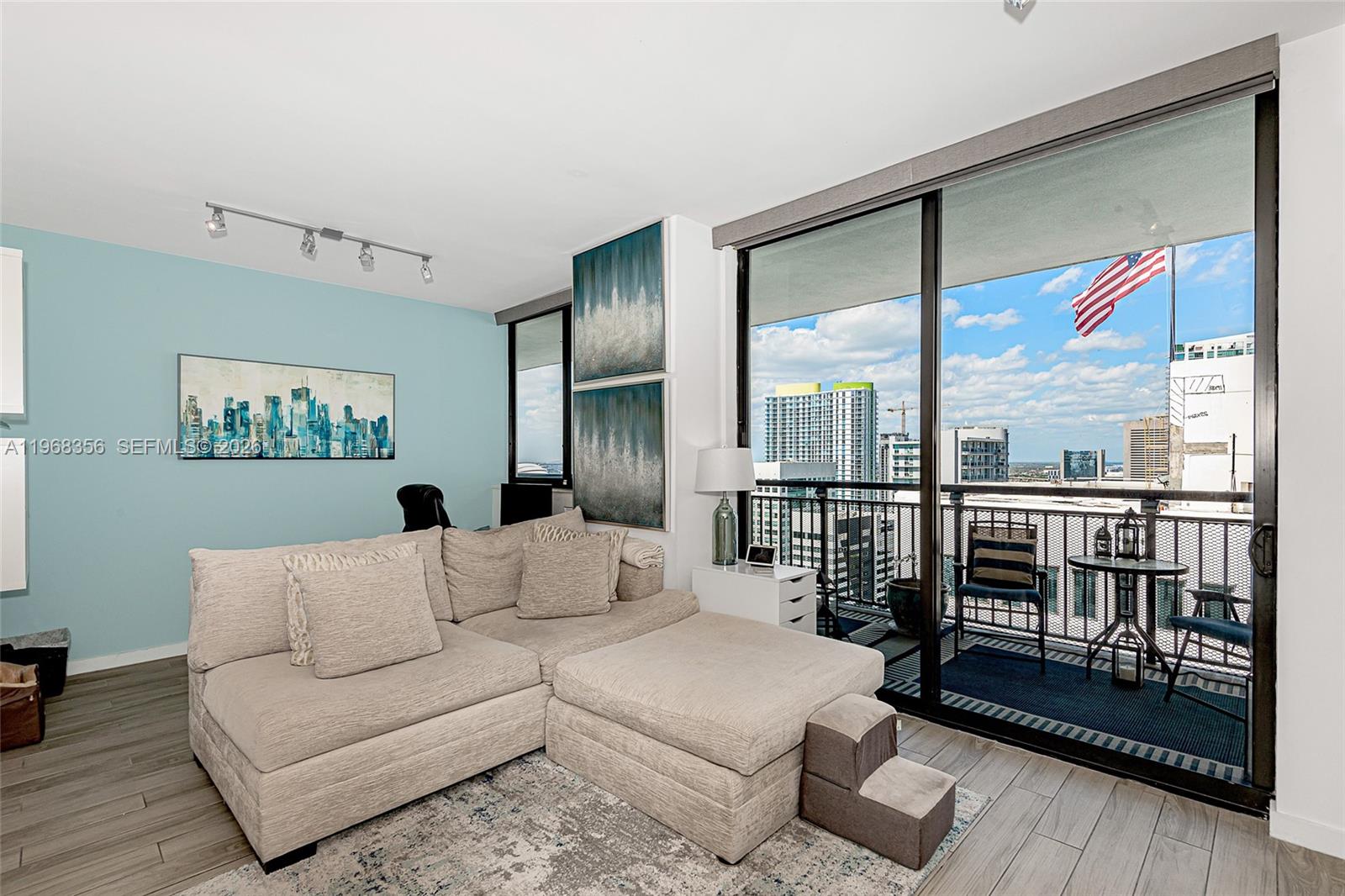 A living room features a beige sectional sofa, light blue walls, and a balcony with city views — 999 SW 1st Ave # 3215, Miami FL 33130, MIAMI, FL