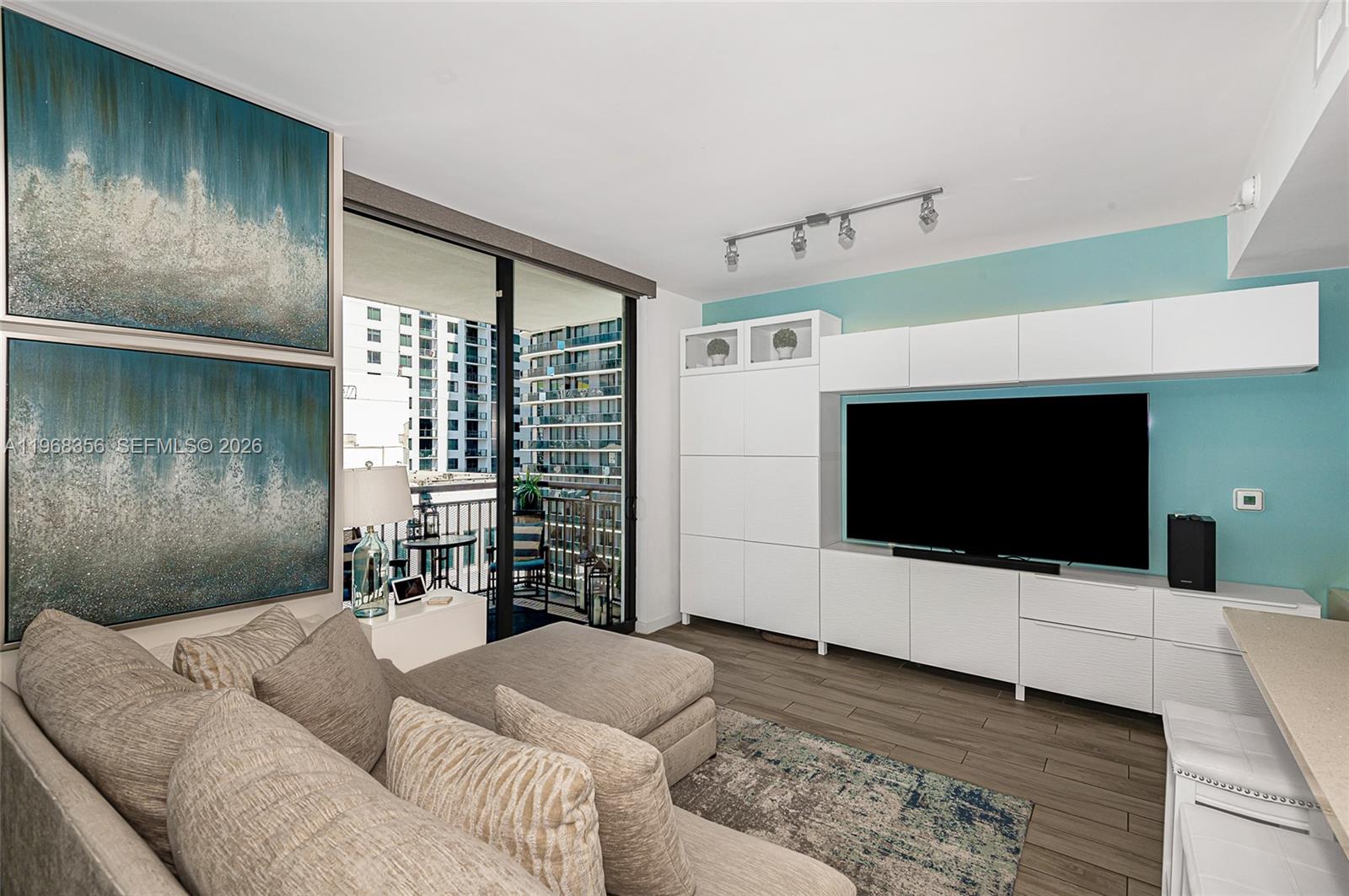 A living room features a large sectional sofa, white media cabinetry, and a balcony view — 999 SW 1st Ave # 3215, Miami FL 33130, MIAMI, FL