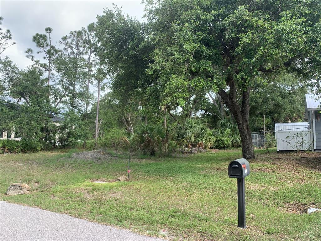 A grassy, wooded vacant lot features a mailbox in the foreground and mature trees — 17505 CLOVER, PORT CHARLOTTE, FL