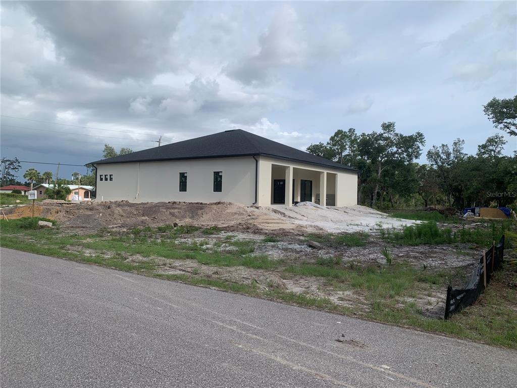 A newly constructed single-story house with a dark roof stands on an unfinished dirt lot — 17505 CLOVER, PORT CHARLOTTE, FL