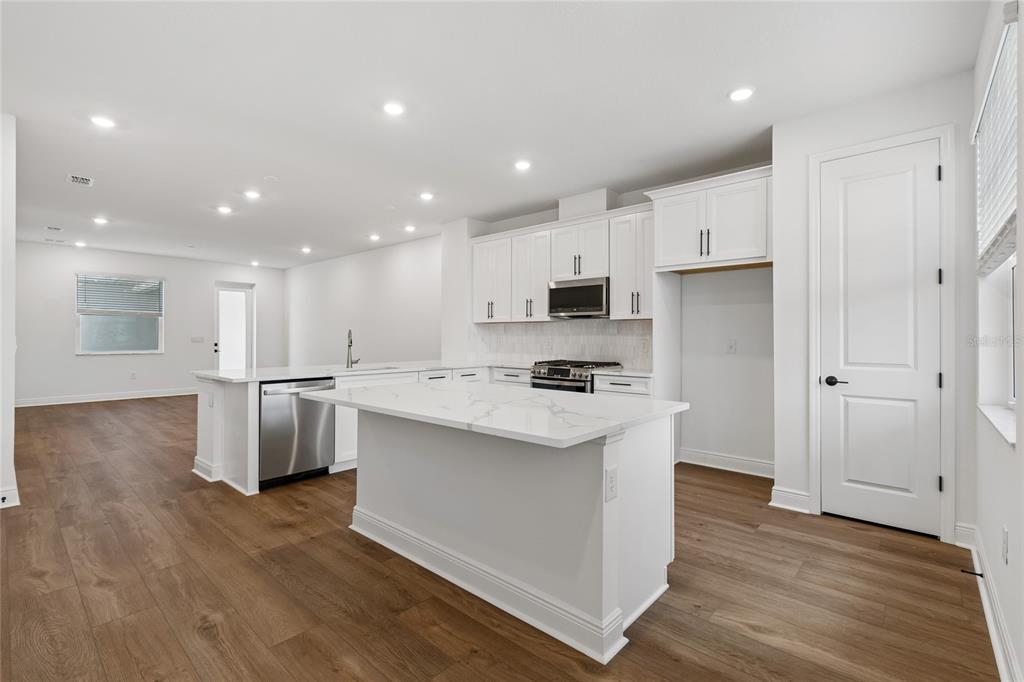 A modern kitchen features white cabinets, a marble-topped island, stainless steel appliances, and wood flooring — 8215 SEAFLOWER PARKWAY, BRADENTON, FL