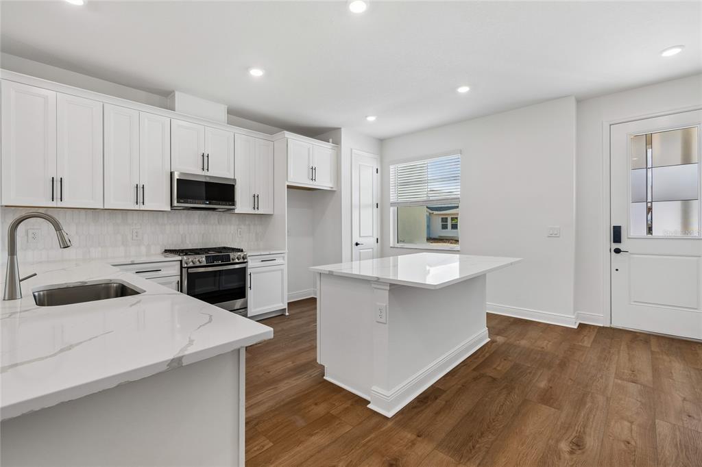 A modern kitchen features white cabinetry, a marble-topped island, stainless steel appliances, and wood flooring — 8215 SEAFLOWER PARKWAY, BRADENTON, FL