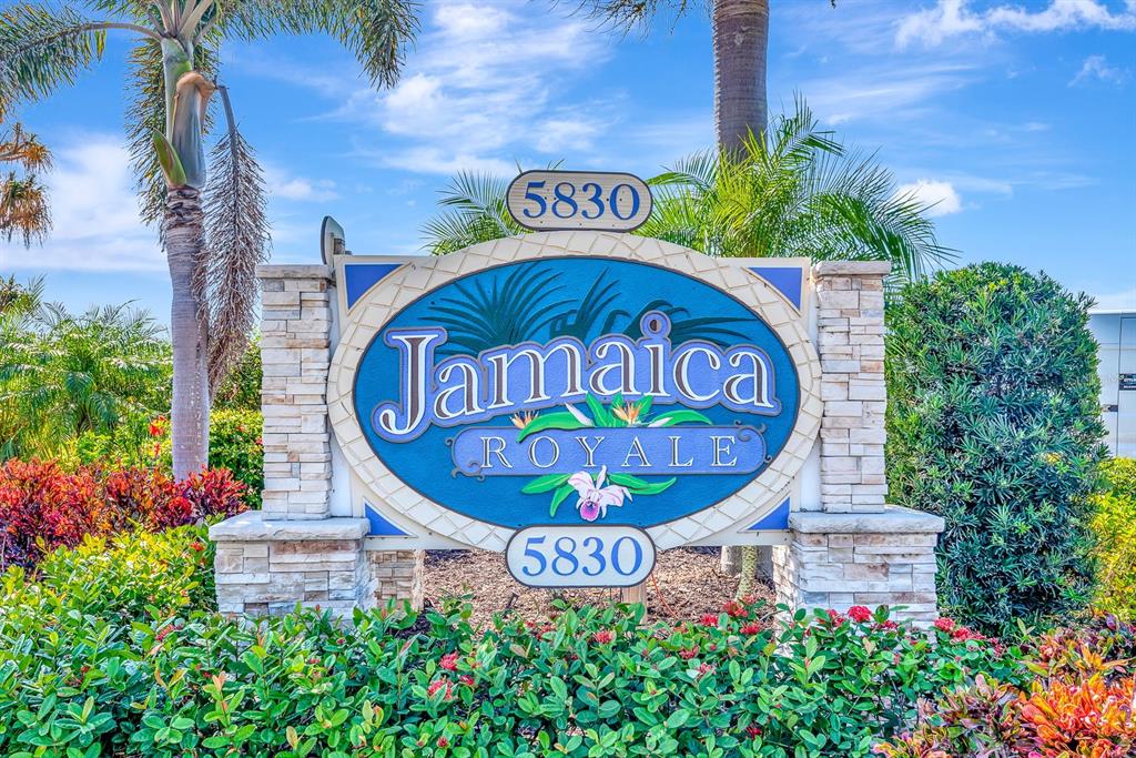 An exterior view of a single-story apartment building with parking spaces and blue chairs — 5830 MIDNIGHT PASS ROAD UNIT 61, SARASOTA, FL
