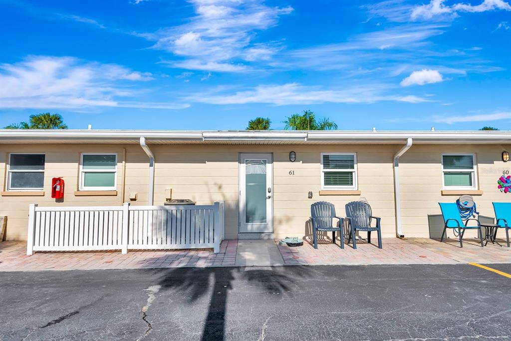 The exterior of a single-story building features a white fence, patio chairs, and unit number 61 — 5830 MIDNIGHT PASS ROAD UNIT 61, SARASOTA, FL