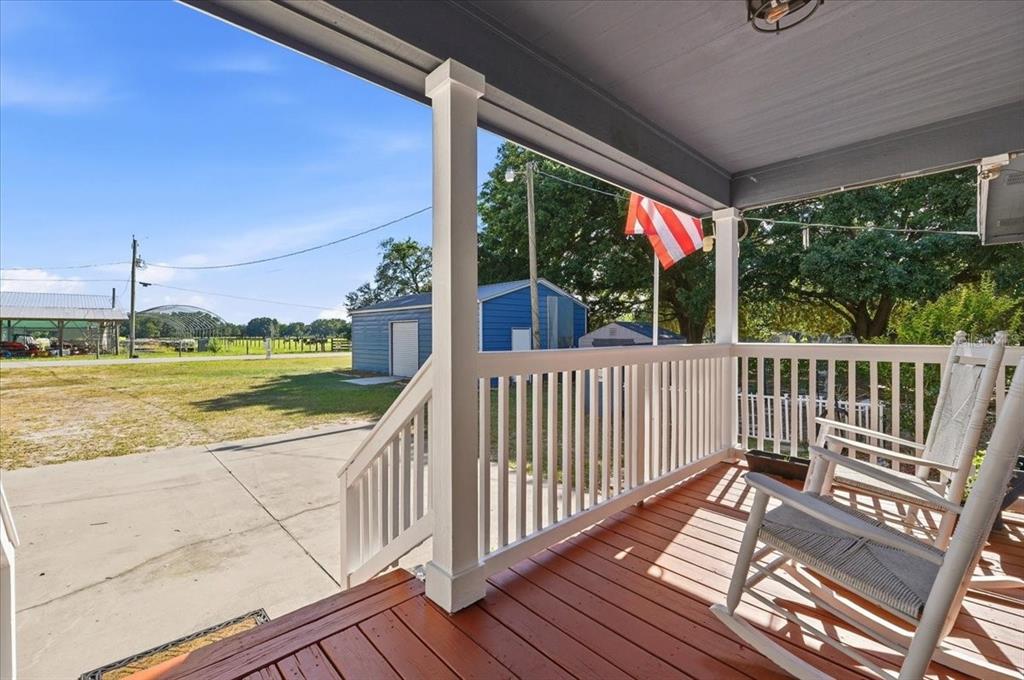 A wooden porch with white railings and rocking chairs overlooks a yard and shed — 10049 QUINN ROAD, POLK CITY, FL