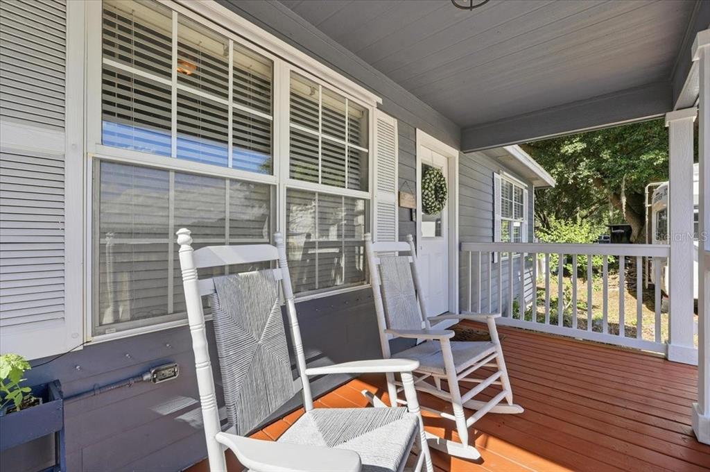 A covered wooden porch features two white rocking chairs in front of a gray house — 10049 QUINN ROAD, POLK CITY, FL