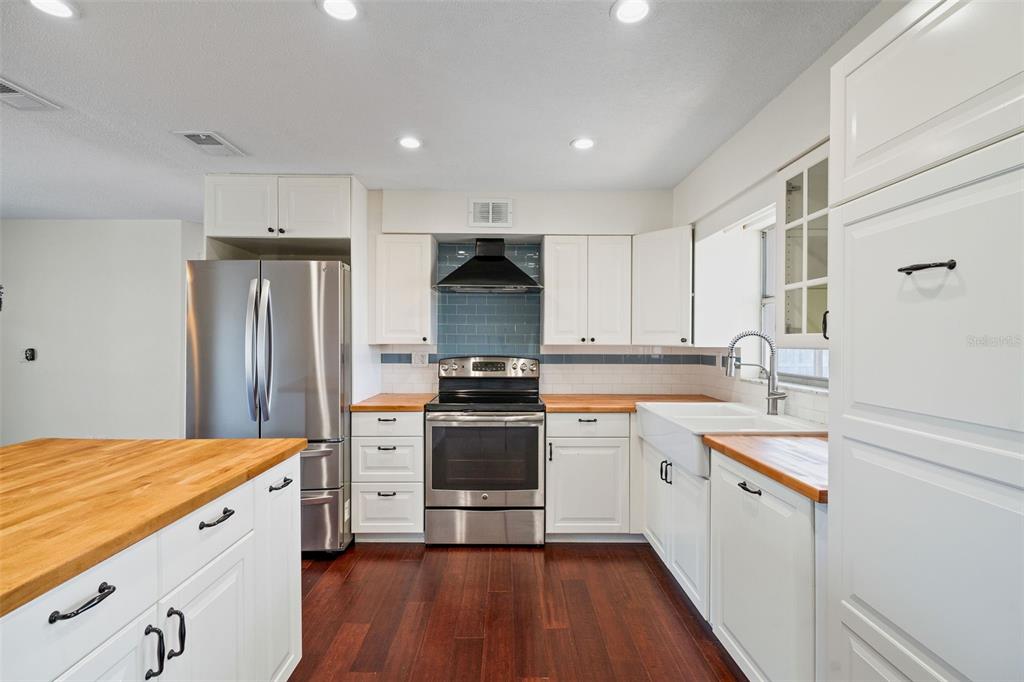 A kitchen features white cabinets, butcher block countertops, stainless steel appliances, and dark wood flooring — 1712 THOMAS DRIVE, CLEARWATER, FL