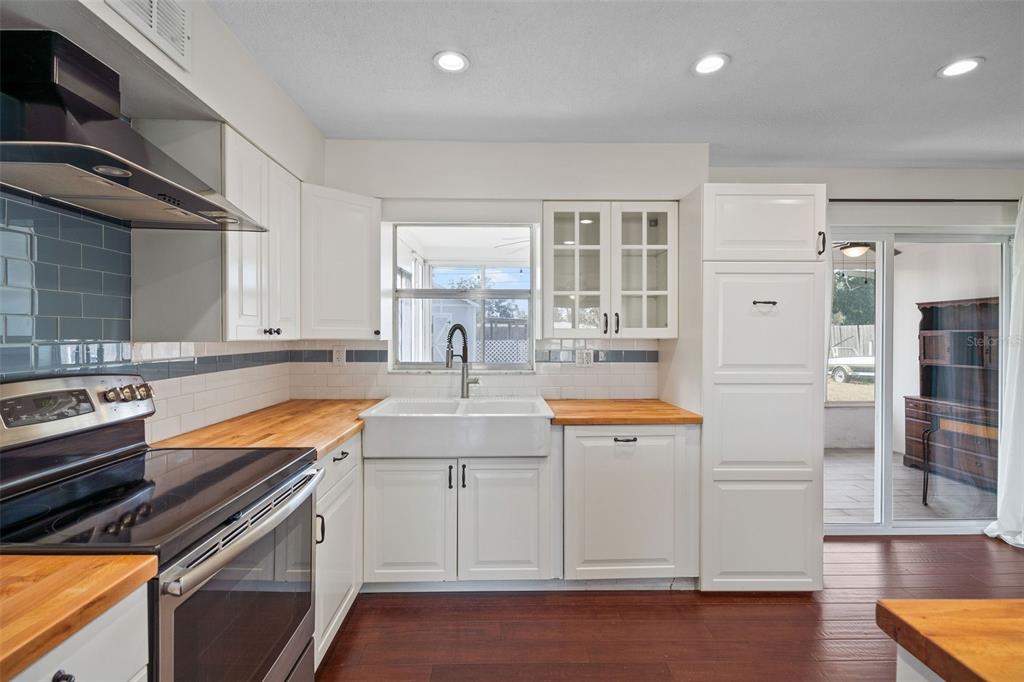 A kitchen features white cabinets, a farmhouse sink, wood countertops, and a blue tile backsplash — 1712 THOMAS DRIVE, CLEARWATER, FL