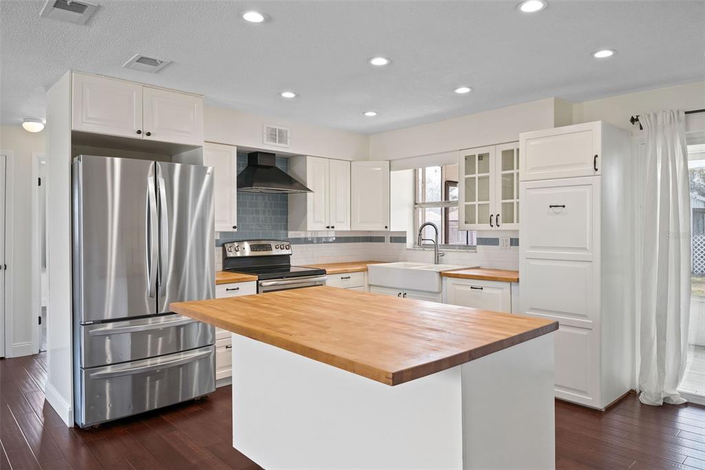 A kitchen features white cabinets, a large wooden island, stainless steel appliances, and dark flooring — 1712 THOMAS DRIVE, CLEARWATER, FL