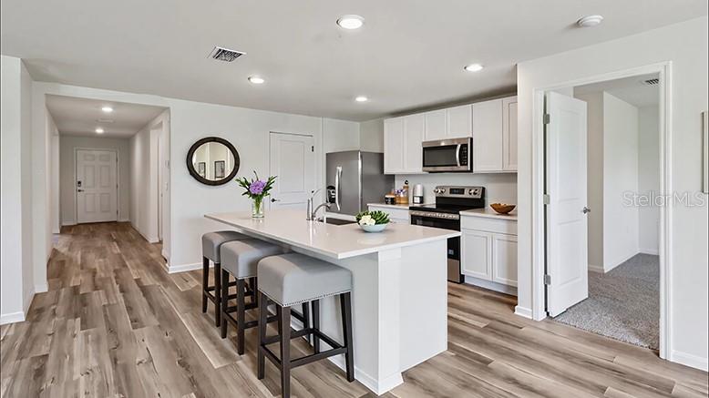 A modern kitchen features white cabinetry, a quartz-topped island with bar stools, and wood-look flooring — 8717 BARRAGAN DRIVE, WILDWOOD, FL