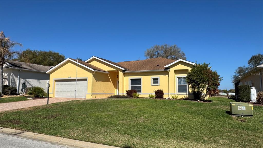 A yellow single-story house with a two-car garage and a front lawn under clear skies — 5024 LONG MEADOW DRIVE, LEESBURG, FL