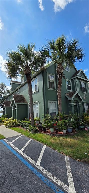 A three-story green building with two palm trees and potted plants in the front yard — 9306 LAKE CHASE ISLAND WAY, TAMPA, FL