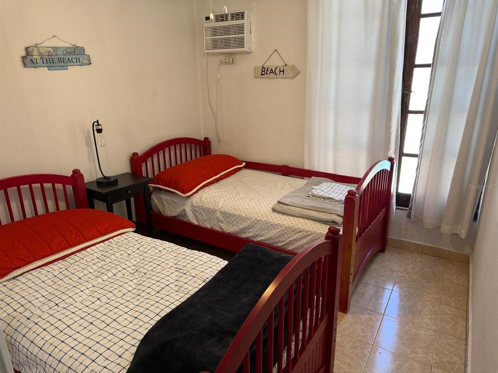 A bedroom features two red wooden twin beds, a nightstand, and a window with curtains — R88 CALLE 7, CAROLINA, PR