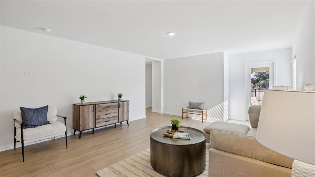 A living room features light wood-look flooring, white walls, a wooden console, and neutral furniture — 5290 BERRY BAY AVENUE, WIMAUMA, FL