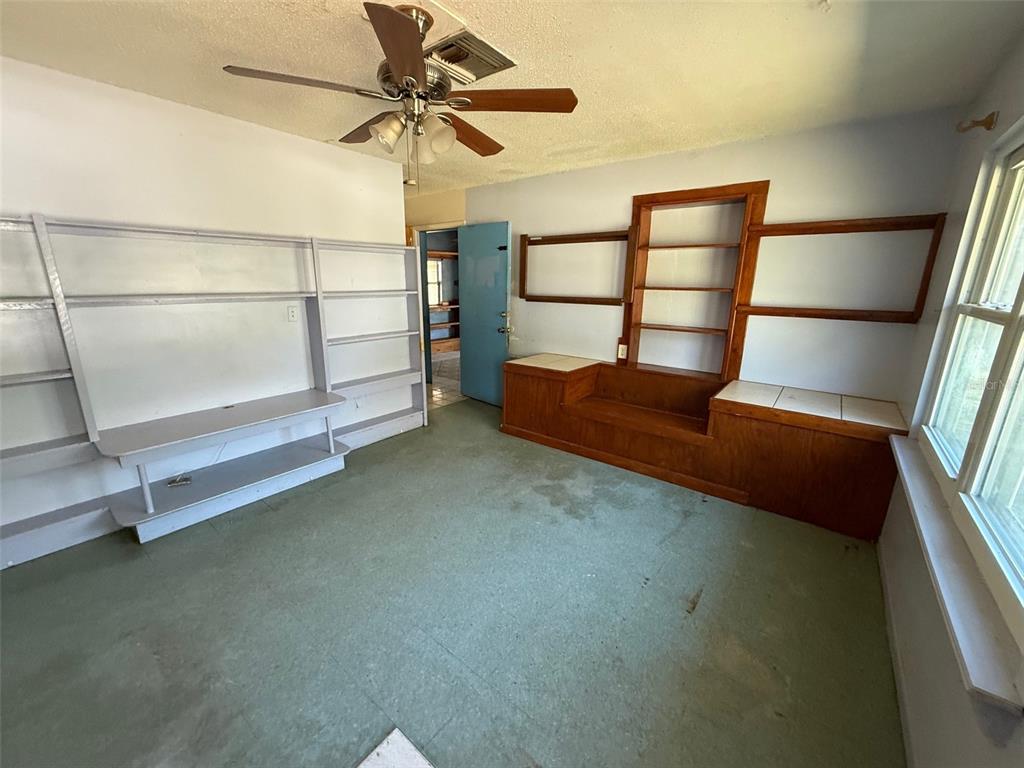 A room with green flooring, a ceiling fan, built-in wooden shelving, and white wall shelves — 6292 W PARK DRIVE, HOMOSASSA, FL