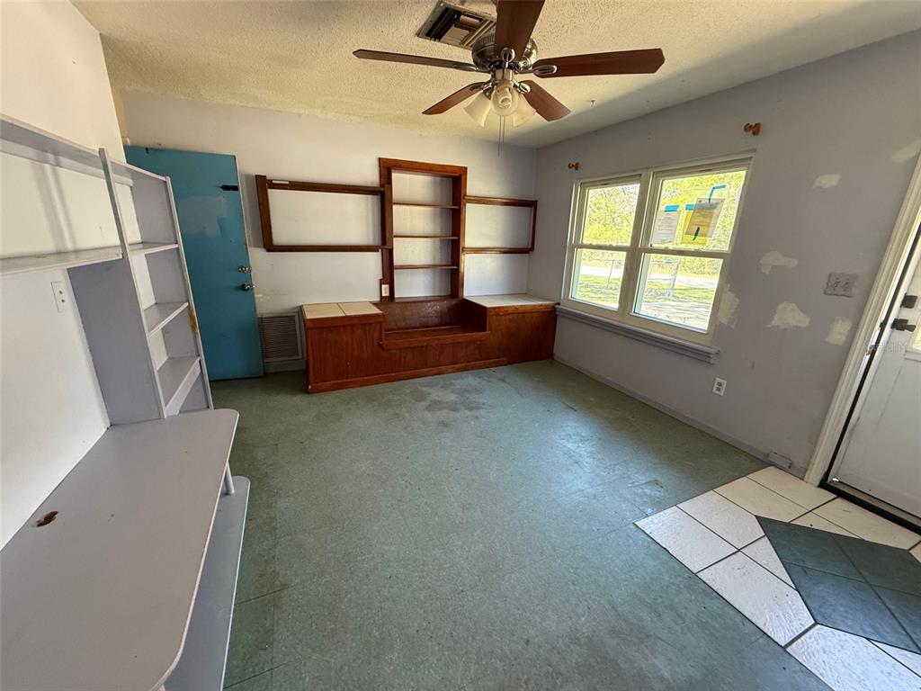 A room with green flooring, a ceiling fan, built-in wooden shelving, and a blue door — 6292 W PARK DRIVE, HOMOSASSA, FL