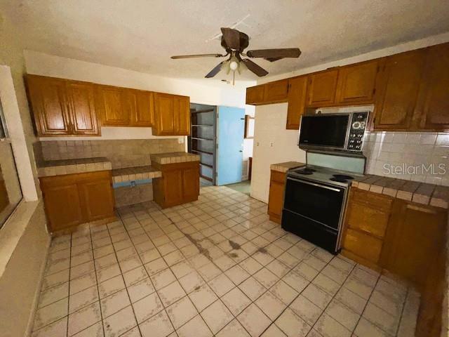 A kitchen features wooden cabinets, tiled countertops, a black stove, and light-colored floor tiles — 6292 W PARK DRIVE, HOMOSASSA, FL