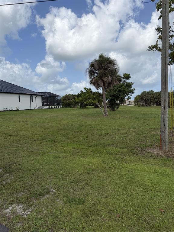 A grassy vacant lot features a single palm tree and an adjacent house with a lanai — 17157 SARONG LANE, PUNTA GORDA, FL