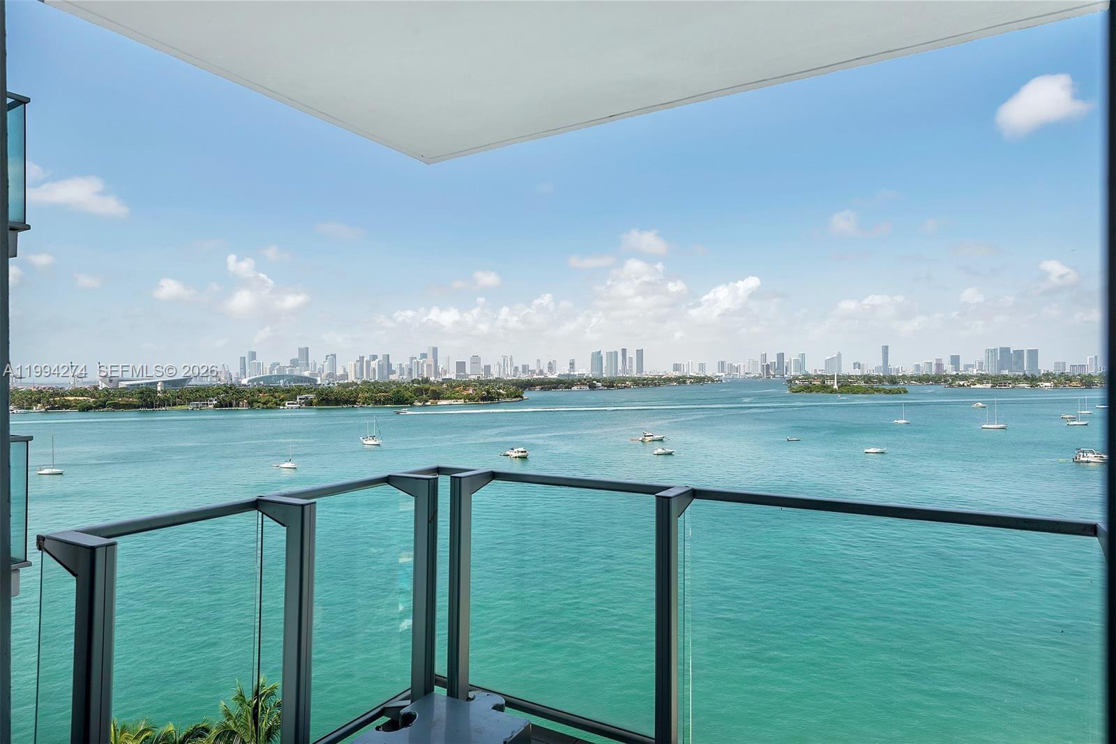 A balcony with a glass railing overlooks a bay with boats and a city skyline — 1100 West Ave # 1020, Miami Beach FL 33139, MIAMI BEACH, FL