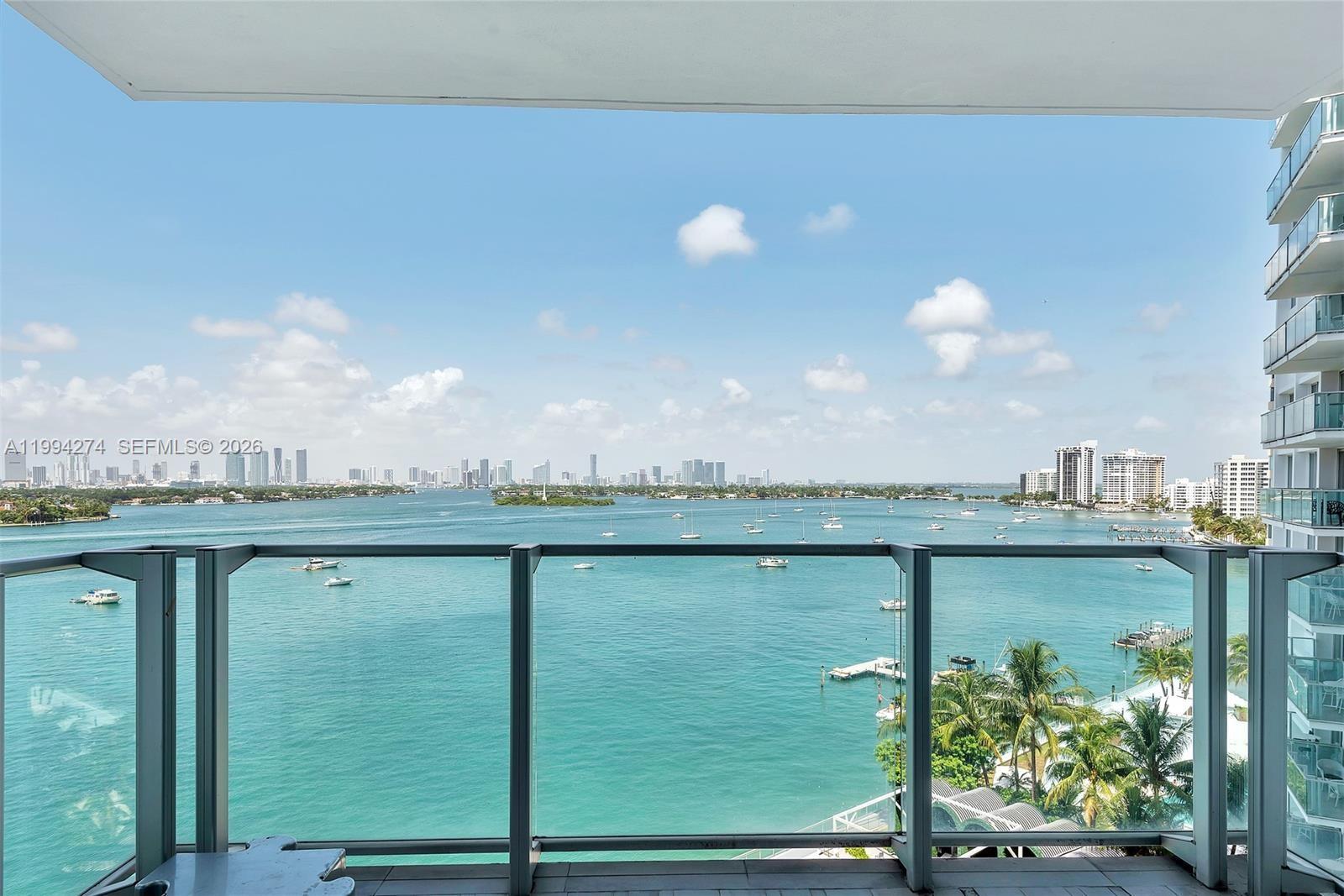 A balcony overlooks a bay with boats and a distant city skyline — 1100 West Ave # 1020, Miami Beach FL 33139, MIAMI BEACH, FL