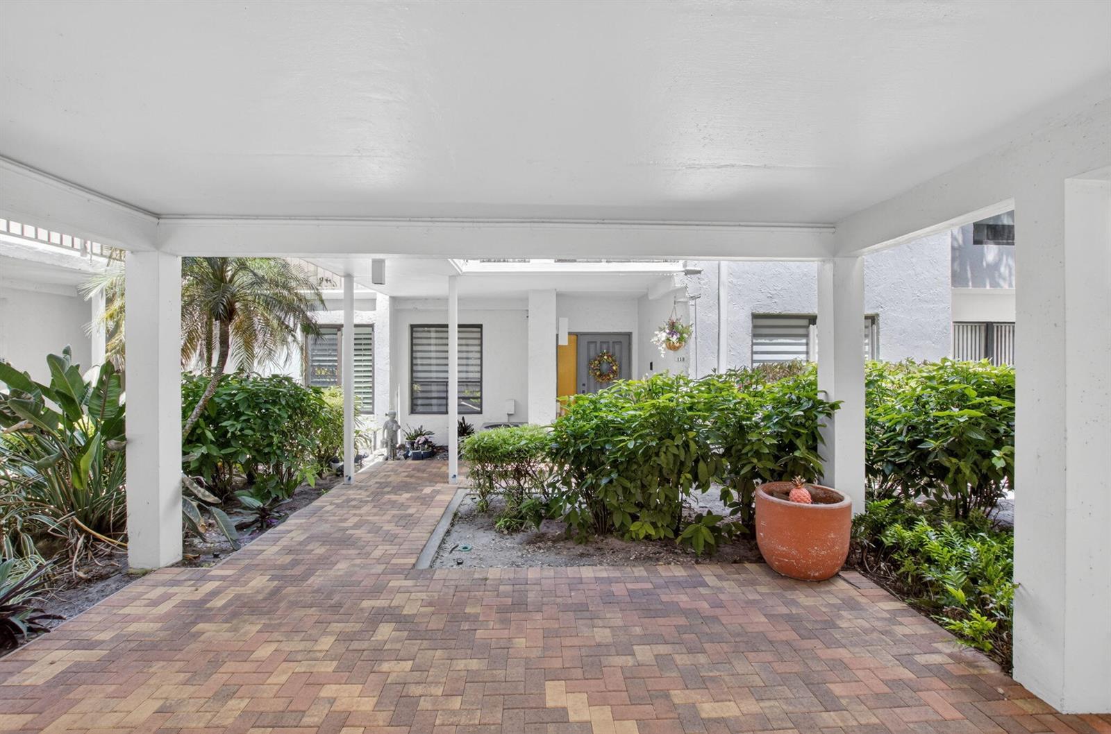 A paved walkway leads under a covered carport toward the front entrance of a building — 900 Greensward Lane # G110, Delray Beach FL 33445, DELRAY BEACH, FL
