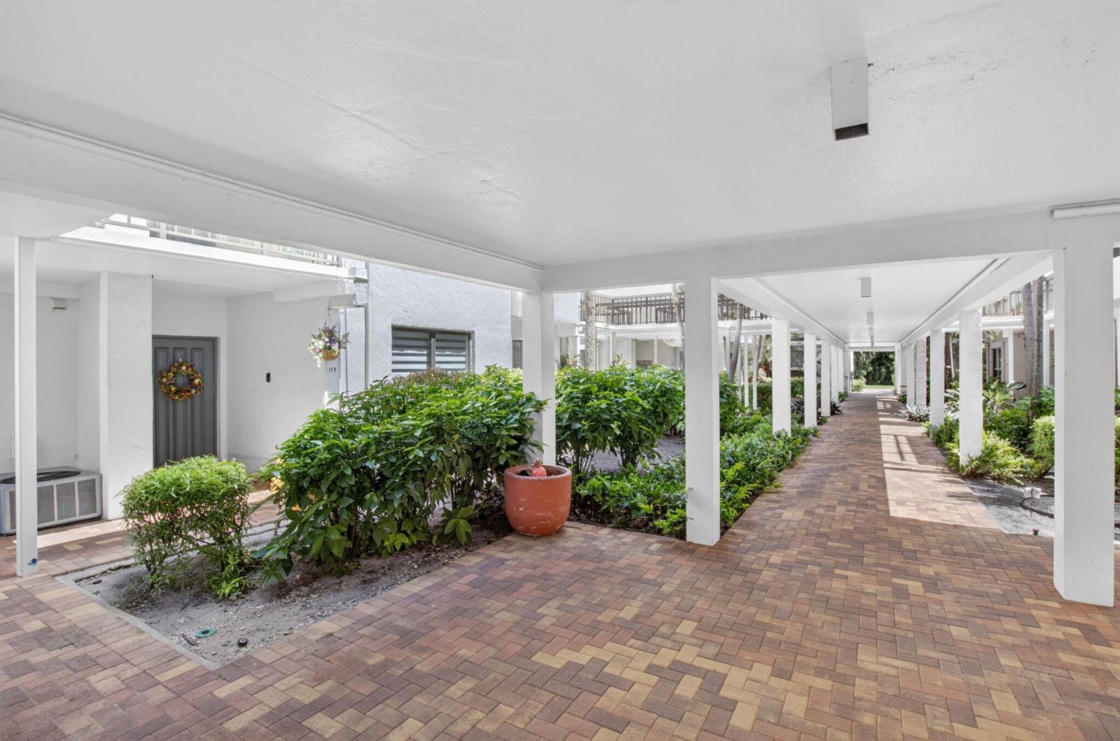 A covered brick walkway leads past a landscaped garden and a residential entrance — 900 Greensward Lane # G110, Delray Beach FL 33445, DELRAY BEACH, FL