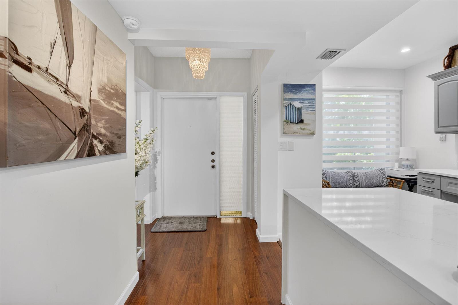 A bright entryway features hardwood floors, a white front door, and a modern chandelier — 900 Greensward Lane # G110, Delray Beach FL 33445, DELRAY BEACH, FL