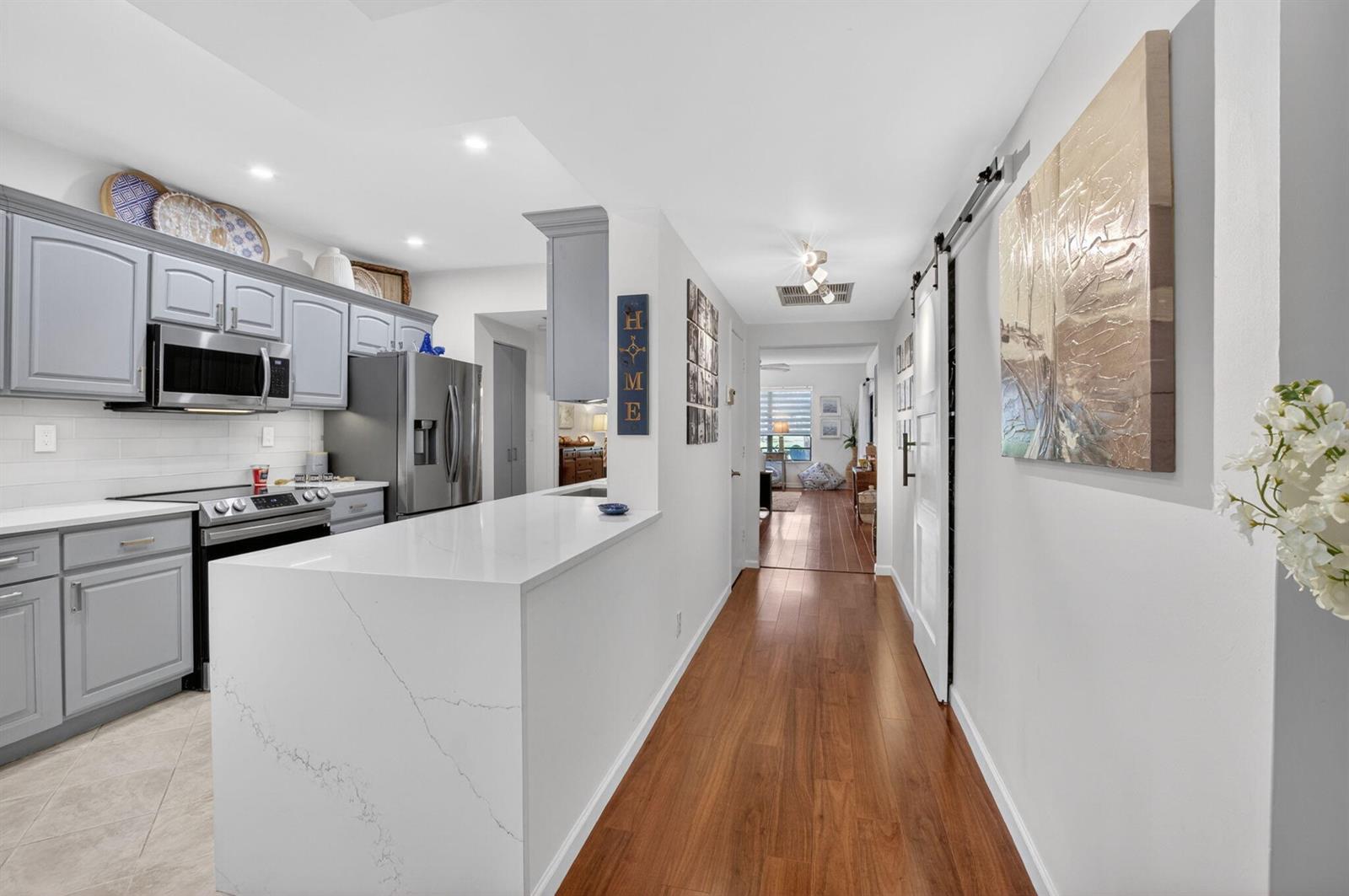 A kitchen with gray cabinets and a white quartz island opens into a hallway — 900 Greensward Lane # G110, Delray Beach FL 33445, DELRAY BEACH, FL