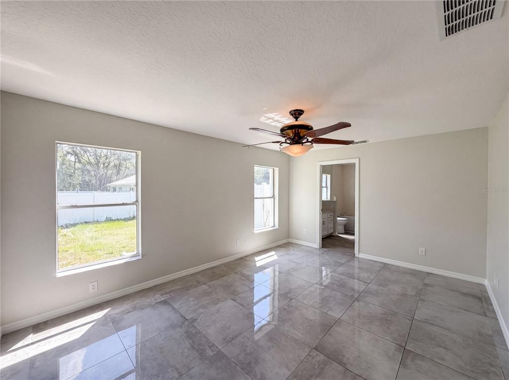 A bedroom with gray tile flooring, a ceiling fan, and an attached bathroom — 6297 SW 148TH STREET, OCALA, FL