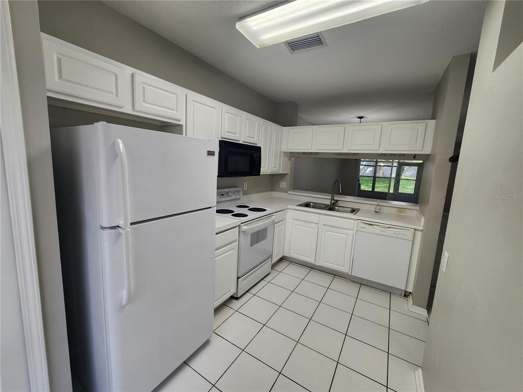 A kitchen features white cabinets, white appliances, tiled flooring, and a pass-through window — 2302 LAKE WOODBERRY CIRCLE, BRANDON, FL