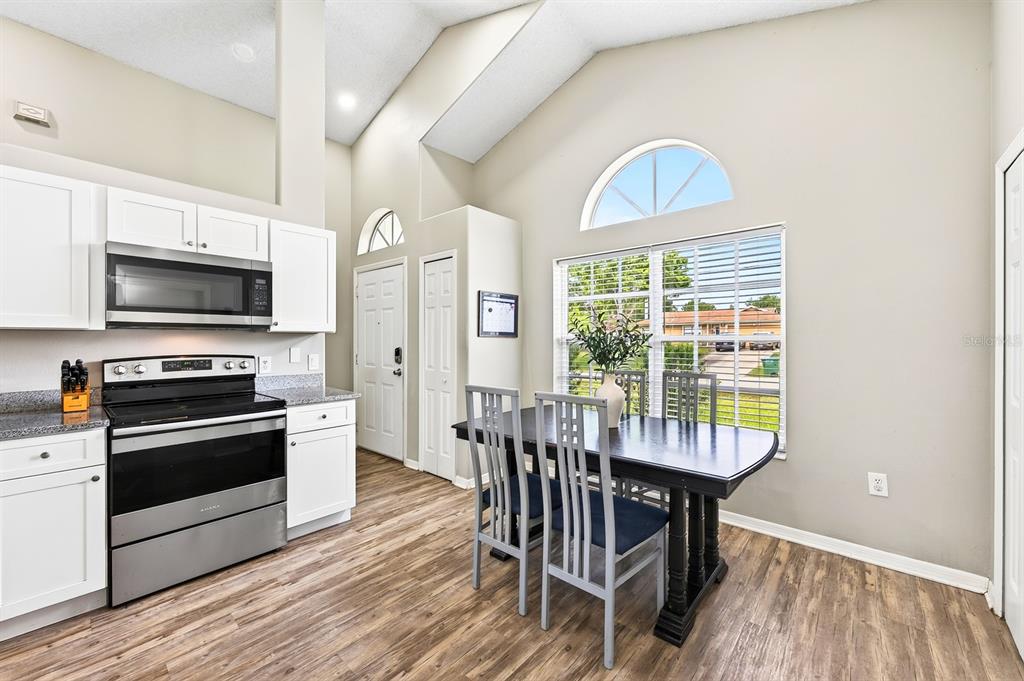 A kitchen and dining area with white cabinets, stainless steel appliances, and vaulted ceilings — 2911 MALCOLM DRIVE, DELTONA, FL