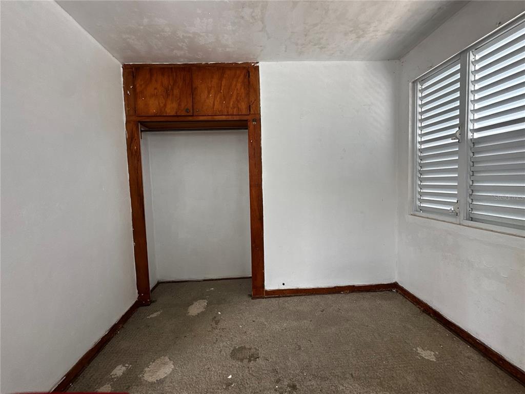 An empty bedroom features white walls, a brown wooden closet frame, and worn gray carpeting — D URB. EL EDEN D-7, COAMO, PR
