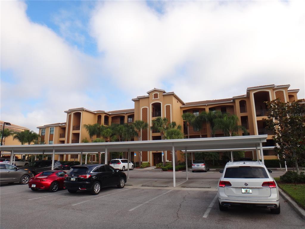 A multi-story apartment building with a covered parking structure in the foreground — 6519 GRAND ESTUARY TRAIL UNIT 307, BRADENTON, FL