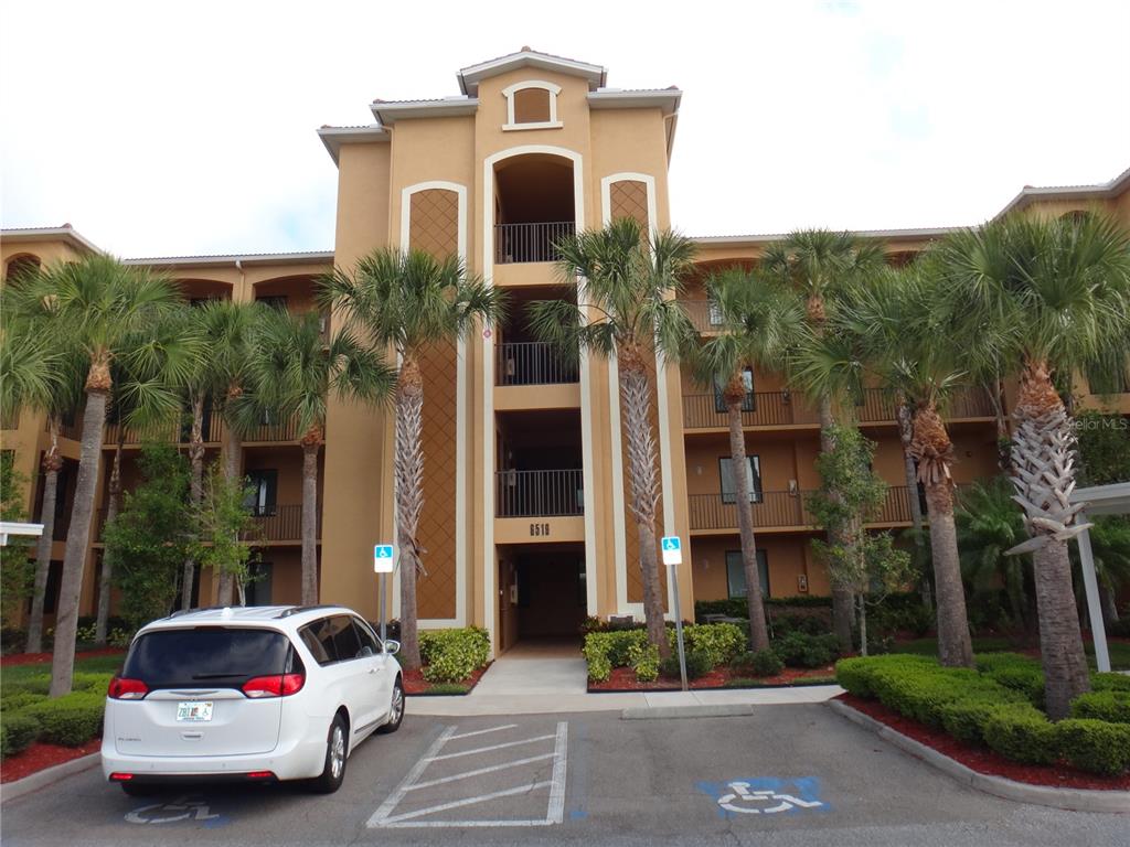 A multi-story tan apartment building with palm trees and a parking lot in front — 6519 GRAND ESTUARY TRAIL UNIT 307, BRADENTON, FL