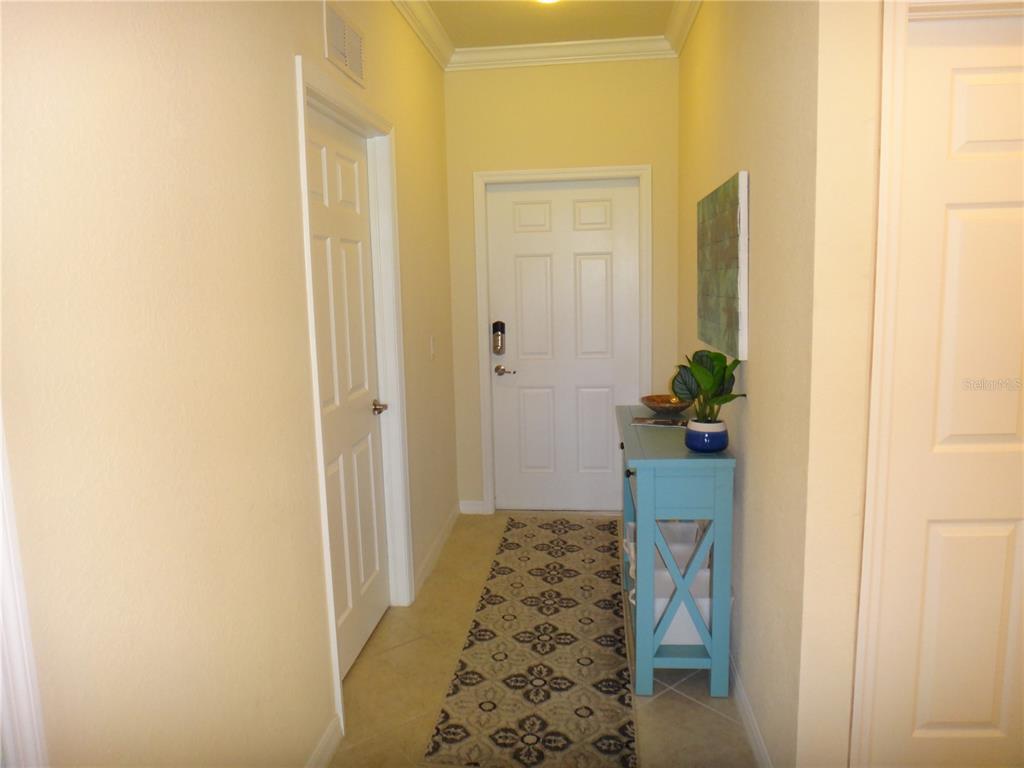 An entryway features a white door, a blue console table, and a patterned runner rug — 6519 GRAND ESTUARY TRAIL UNIT 307, BRADENTON, FL