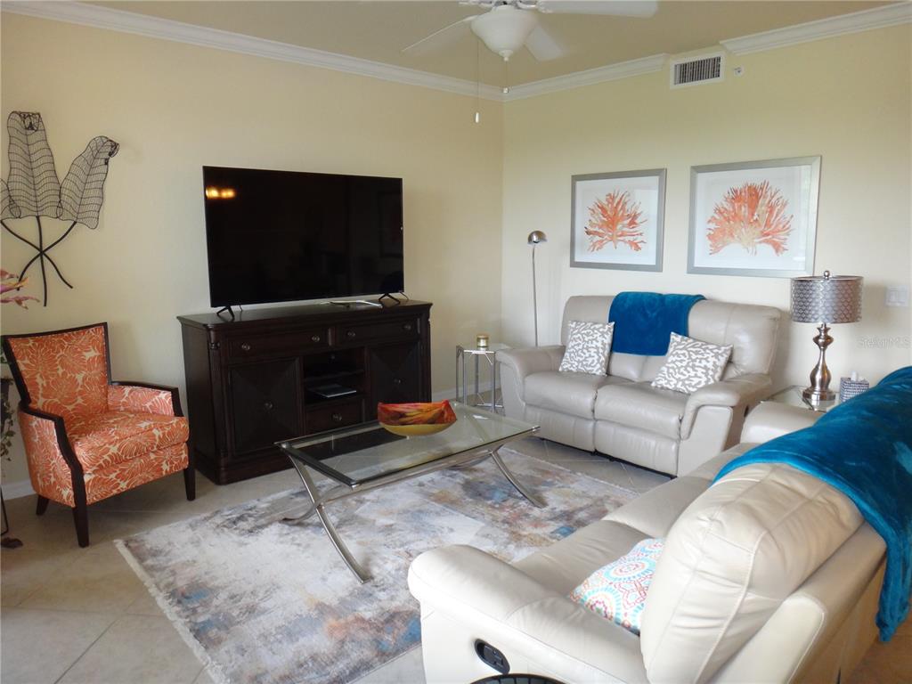 A living room features a television on a dark console, two leather sofas, and chairs — 6519 GRAND ESTUARY TRAIL UNIT 307, BRADENTON, FL