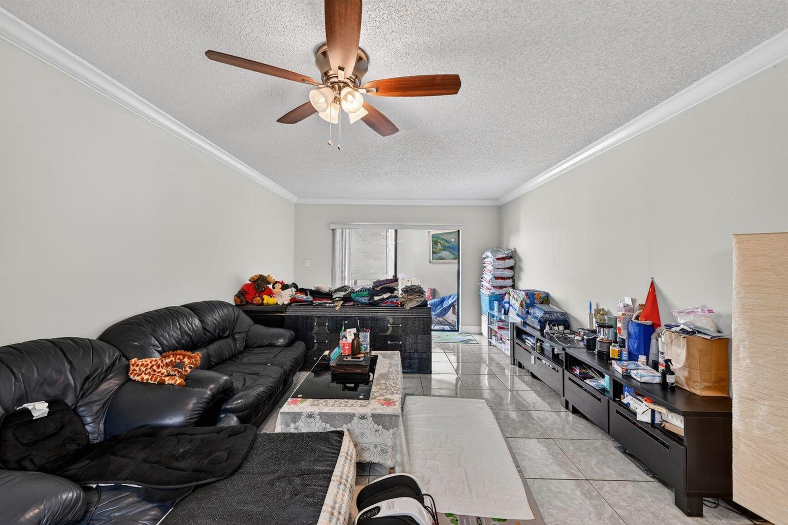 A living room with tile floors, a ceiling fan, a black sofa, and storage furniture — 8290 Lake Drive # 305, Doral FL 33166, DORAL, FL