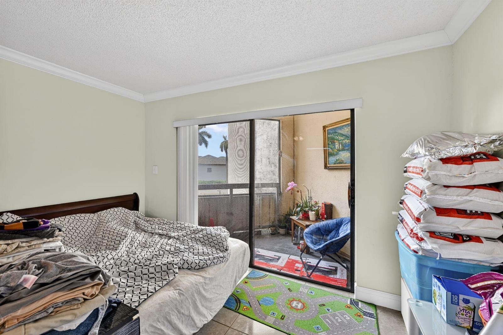 A bedroom with a bed, a sliding glass door to a balcony, and stacked storage bins — 8290 Lake Drive # 305, Doral FL 33166, DORAL, FL