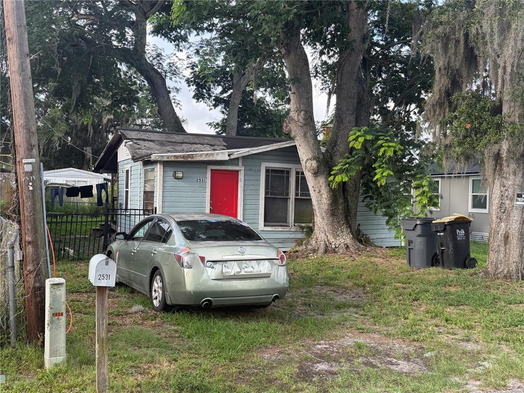 A light blue house with a red door sits behind a silver sedan and trees — 2531 WEBER STREET, LAKELAND, FL