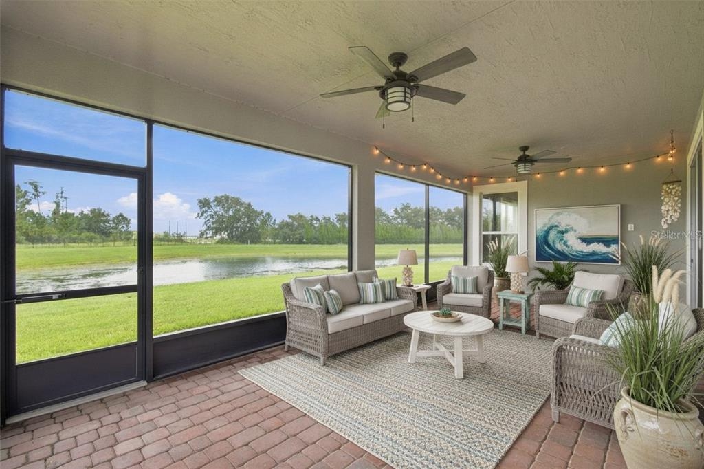 A screened-in patio features wicker furniture, a brick floor, and a view of a pond — 163 OLYMPUS WAY, KISSIMMEE, FL