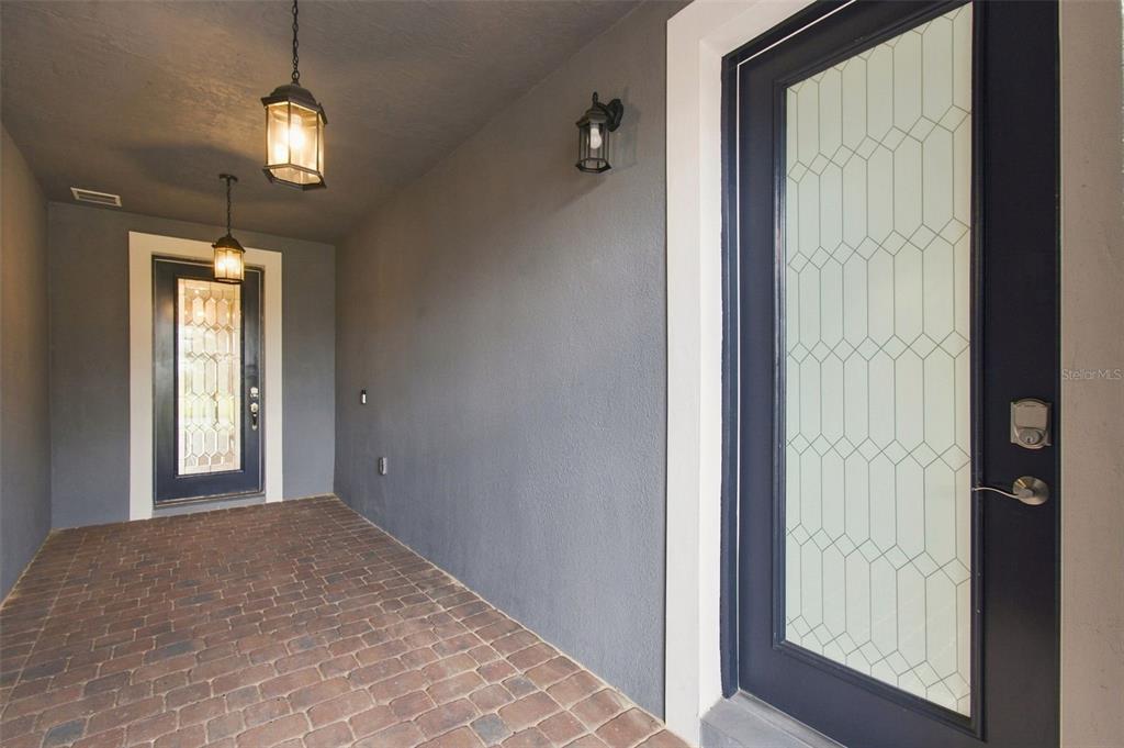 A covered entryway features a brick floor, gray walls, two hanging lanterns, and a glass-paneled door — 163 OLYMPUS WAY, KISSIMMEE, FL