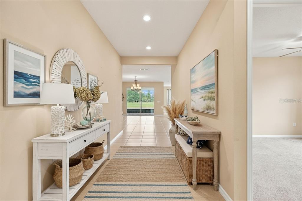 A bright hallway features two console tables, coastal decor, and a view of the backyard — 163 OLYMPUS WAY, KISSIMMEE, FL