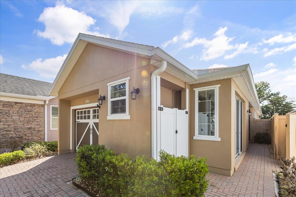 A tan stucco house exterior features a brick paver walkway and a white privacy gate — 126 BAYOU BEND ROAD, GROVELAND, FL