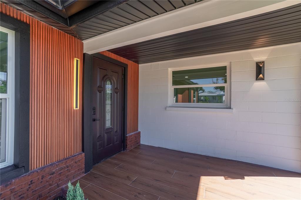 A covered front porch with wood-look tile flooring, a dark door, and vertical wood siding — 1797 BIRCH DRIVE, VENICE, FL