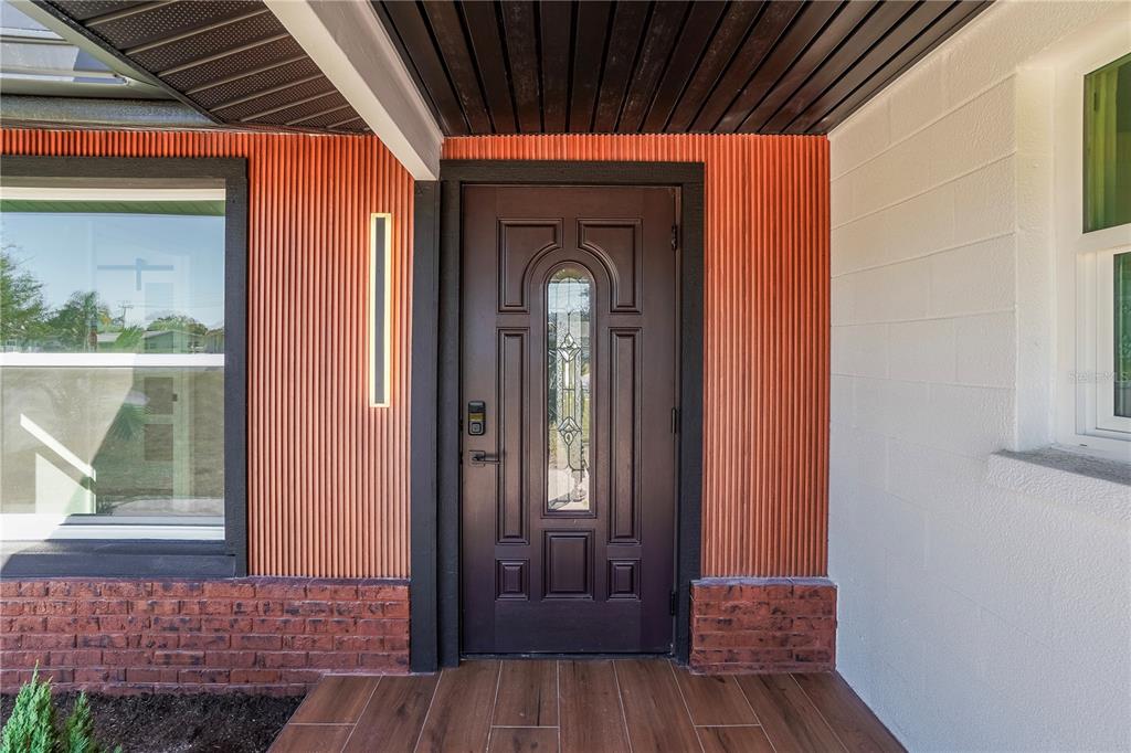 A dark brown front door with a glass insert is set against orange corrugated siding — 1797 BIRCH DRIVE, VENICE, FL