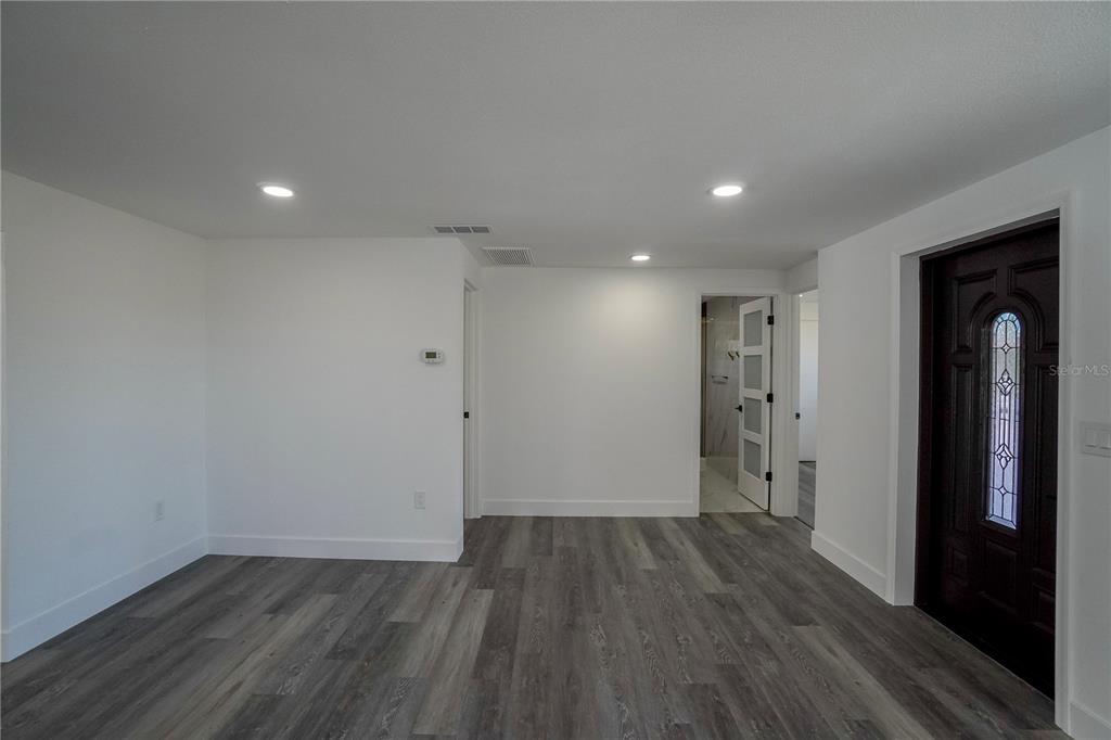 A room with white walls, gray wood-look flooring, recessed lighting, and a dark front door — 1797 BIRCH DRIVE, VENICE, FL