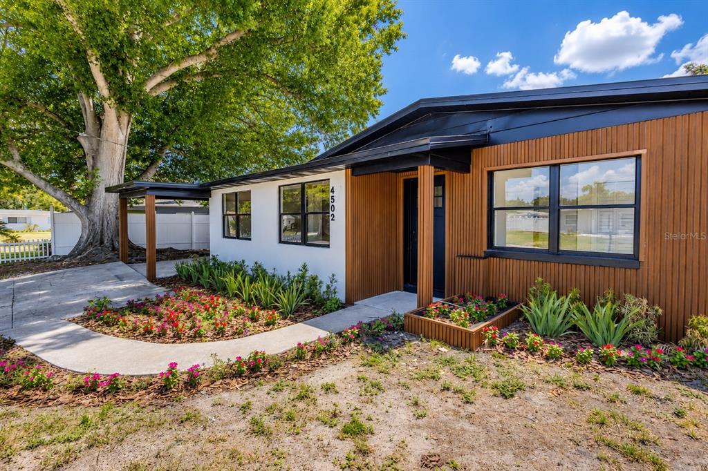 A single-story house exterior features white and wood-paneled siding, a covered entryway, and landscaped flowerbeds — 4502 S GRADY AVENUE, TAMPA, FL