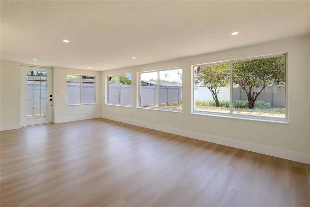 A bright, empty room features light wood-look flooring, white walls, recessed lighting, and large windows — 4502 S GRADY AVENUE, TAMPA, FL